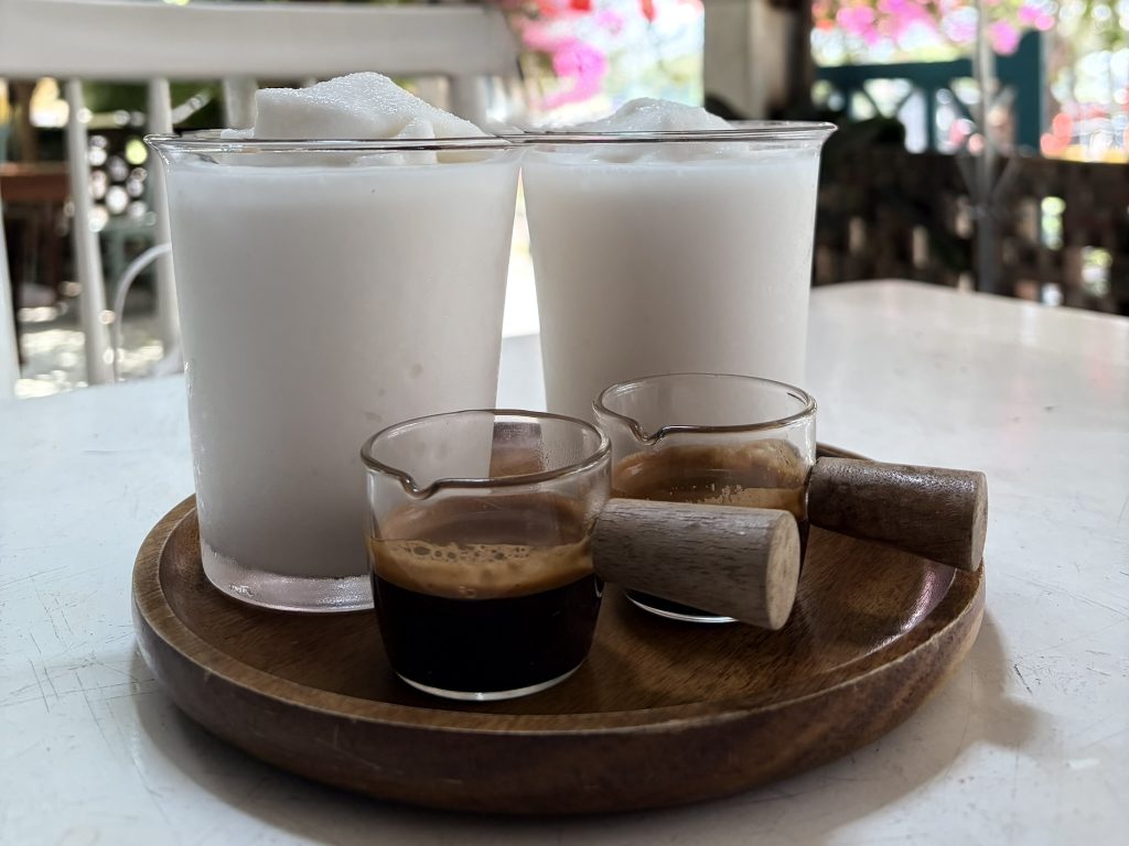 Two coconut coffees are served on a platter on a table with pink flowers in the background