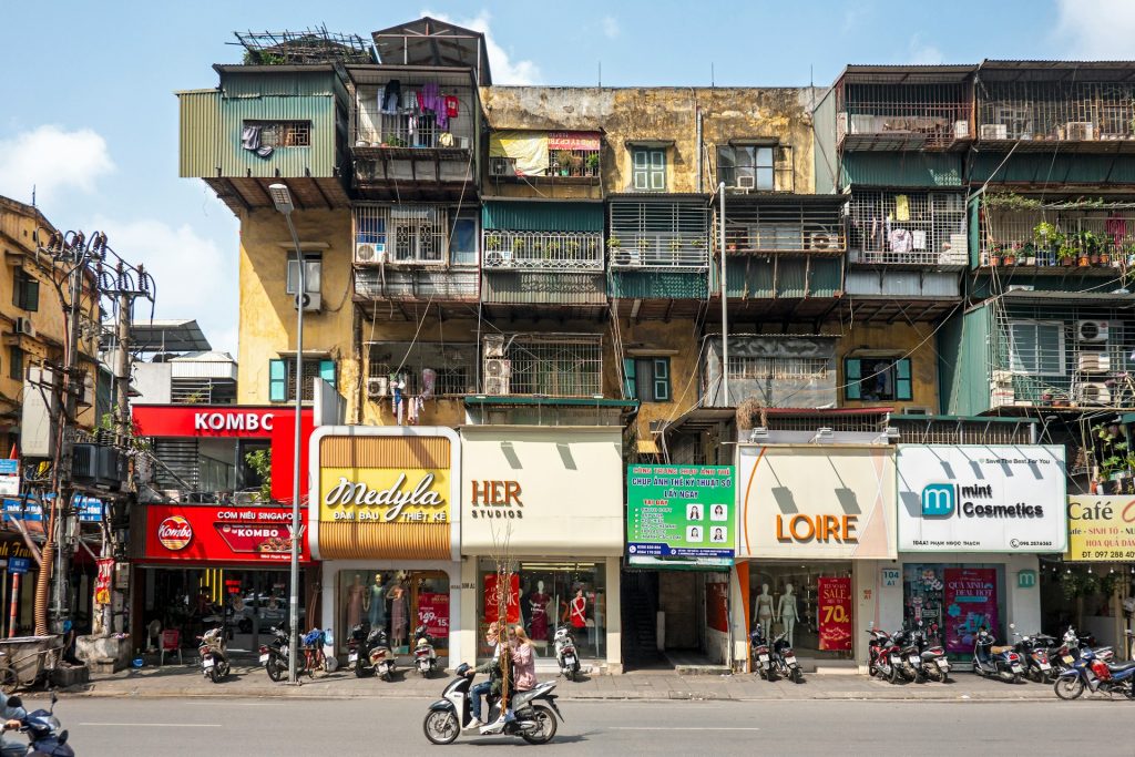 A group of people riding motorcycles down a street with tube houses behind in the Old Quarter
