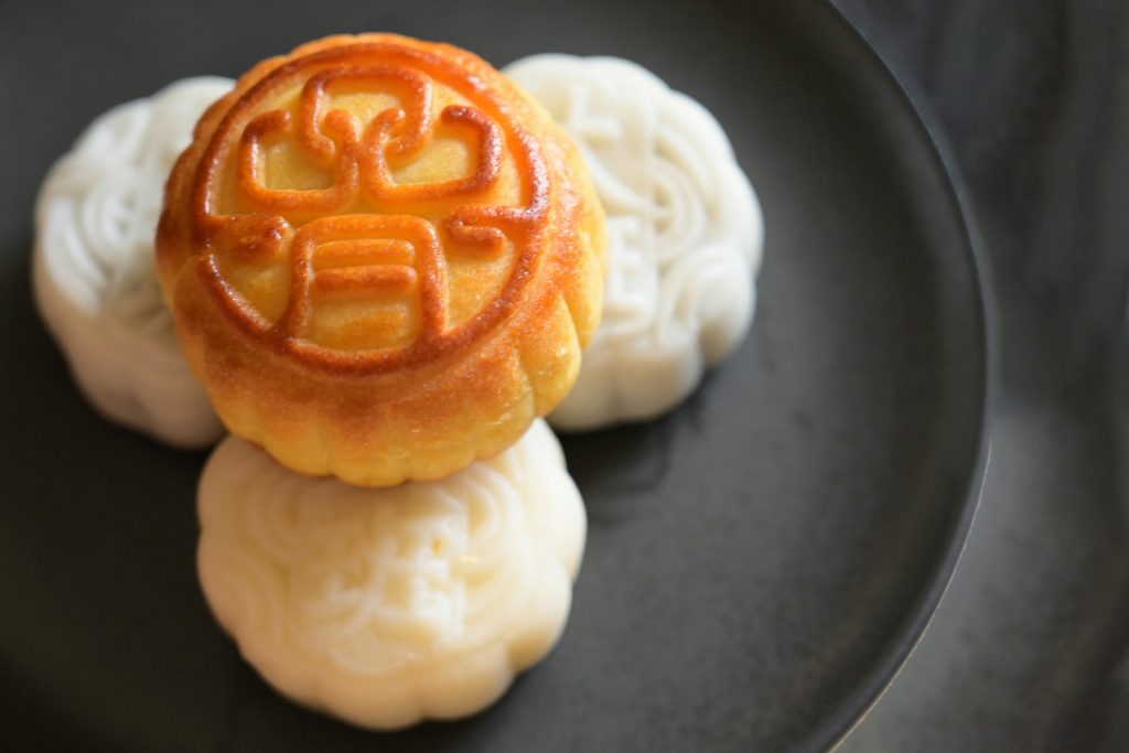 brown and white Vietnamese mooncakes eaten during Mid-Autumn Festival on black round plate