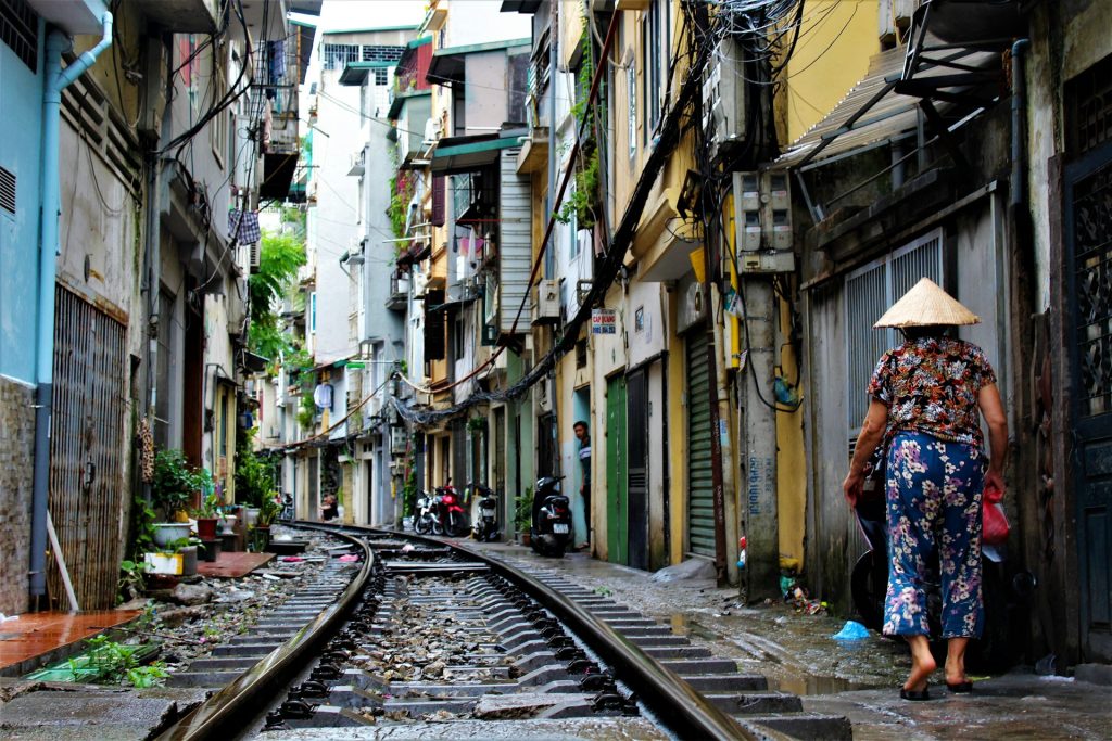 person walking on railway side between buildings at daytime in Hanoi Old Quarter